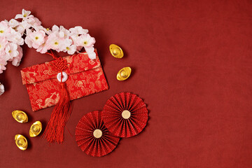 Chinese new year festival decoration over red background. traditional lunar new year red pokets, gold ingots, paper fans, flowers. Flat lay, top view, copy space