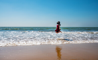 Young woman of indian ethnicity joyfully jumping on paradise beach of Goa ( Unrecognizable person )