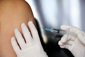 Vaccination during covid-19 pandemic, female hand in protective gloves with syringe. Nurse preparing to injection into a male arm