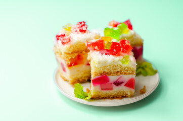A portion of cream cake with pieces of colourful jelly and sprinkled with coconut flakes