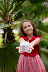 Little girl on a background of palm trees holds a gift in her hands.