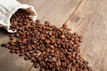 coffee beans are falling from a white sack on an old wooden background. Copy space