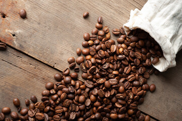 coffee beans are falling from a white sack on an old wooden background. Copy space