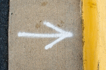 Spray painted arrow on the side of a road pointing to a yellow curb - Powered by Adobe