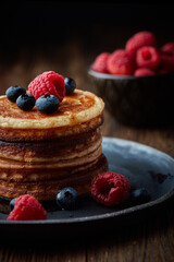 Tasty appetizing homemade pancakes served with honey, raspberries and blueberries on plate on dark background