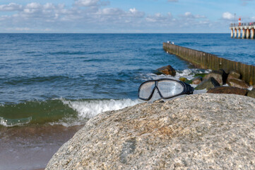 Swimming goggles. Large sea rock. Breakwaters in the sea.