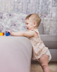 Fototapeta premium Adorable baby stands near the sofa and plays with colored toys