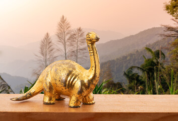 Old gold dinosaur on wood table and on nature background.