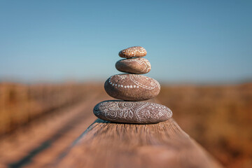 Pila de cuatro piedras redondeadas decoradas con dibujos estilo zen en un paisaje de playa luminoso sobre una repisa de madera