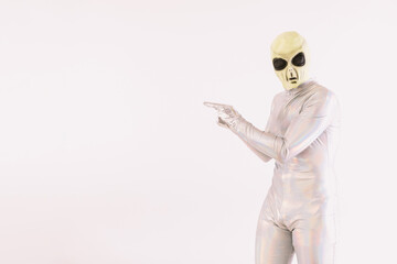 Person dressed in silver suit and green alien mask, pointing with his hands, on white background