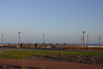 Sunny day with green grass and blue sky. Young trees. Reidi tee promenade. Modern space for walking and rest in a city by the seaside. Lamp posts. Tallinn, Estonia, Europe. November 2021