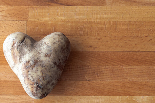 A close up photograph of a raw uncooked heart shaped white potato on a wooden cutting board making a great Valentine's Day or romantic background image with copy space.