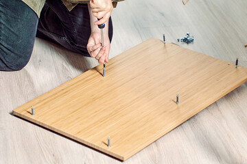 Diy assembling flat pack furniture with screwdriver at home.