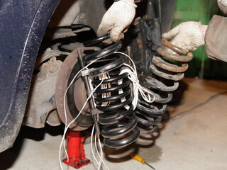 New and old damaged coil springs in repairman hands on broken car on bottle hydraulic jack...