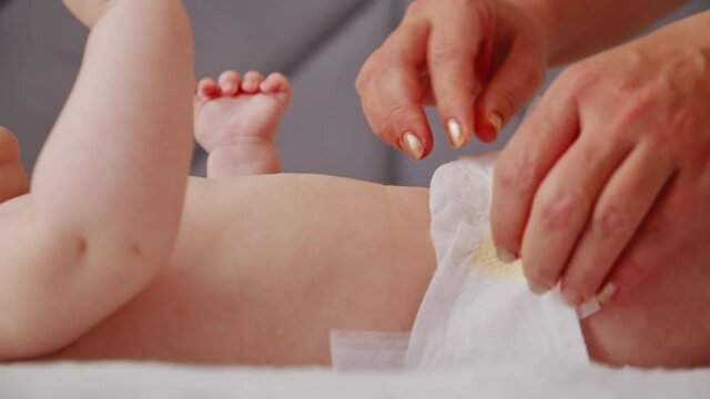 Mother changing diaper on her newborn baby. Mother changing diaper on her newborn baby indoors. The child moves his legs.  Dry skin.  Mom puts diapers on her newborn baby on a changing table.
