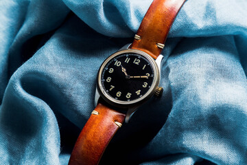 Blue fabric background and on this Watch with black dial and ivory-tone numbers, honey-colored...