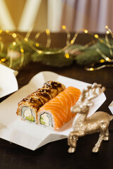 Sushi roll on the new year lights background. Christmas lights decoration. Food delivery at new year eve. Roll with salmon, eel, avocado and soft cheese.