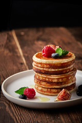 Tasty appetizing homemade pancakes served with honey, raspberries and blueberries on plate on dark background