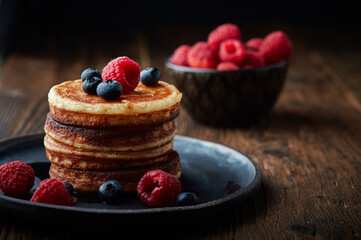 Tasty appetizing homemade pancakes served with honey, raspberries and blueberries on plate on dark background