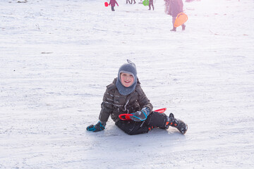 Fototapeta na wymiar Young child, is happy, having fun, sledding on saucer like object, down snowy hillside in winter.