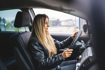 Young adult one caucasian woman driving car waiting while holding wheel looking on the road side view female driver copy space real people