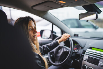 Naklejka premium Young adult one caucasian woman driving car waiting while holding wheel looking to the side back view female driver copy space real people