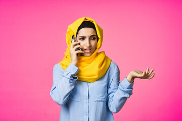 muslim woman in yellow hijab talking on the phone technology pink background