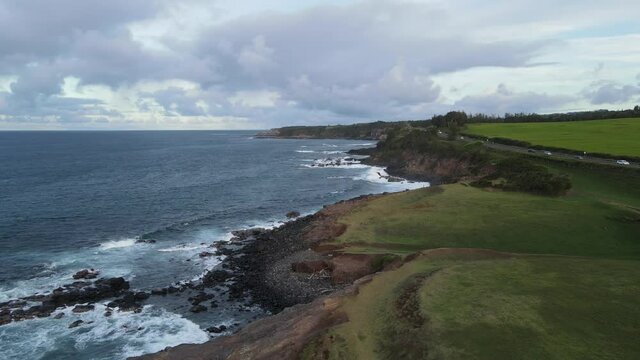 Aerial drone video of the beautiful island paradise of Maui Hawaii with blue ocean waves crashing on rocks of lush green coastline at sunset with mountains in the background 4K HD