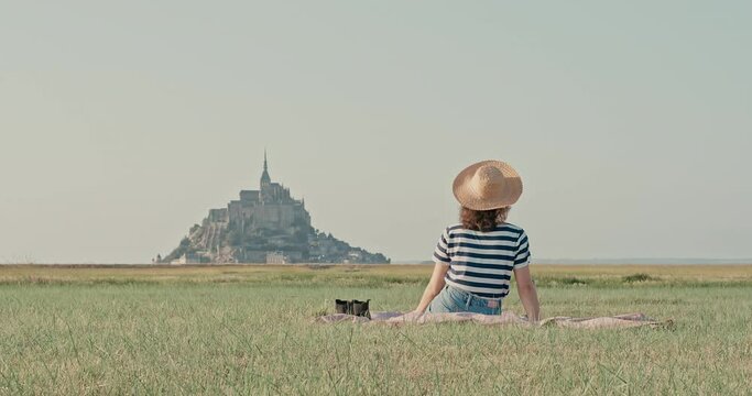 Young woman wearing hat picknick drink wine in front of mont saint michel shot in 4k super slow motion