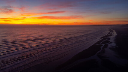 Aerial view captured by drone of the Pacific ocean beach under a vibrant colored red and orange sky during sunset