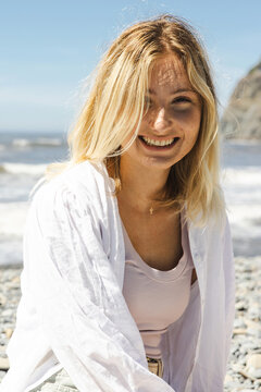 Pretty young woman with blonde hair and radiant smile outside at the ocean beach