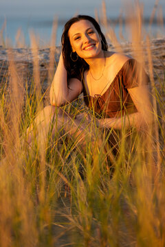 Pretty teenage girl sitting in tall grass outside during the golden hour
