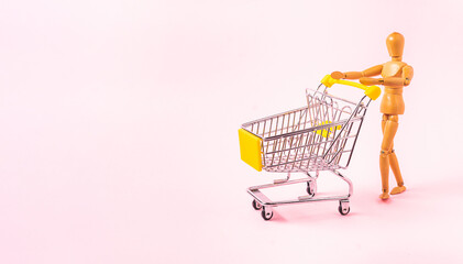 wooden human figure with a miniature shopping car isolated on a pink background