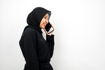 Beautiful young asian muslim woman smiling confidently and cheerfully calling someone, facing empty space, isolated on white background, advertising concept