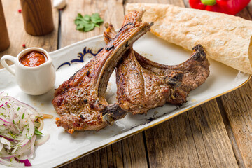 Rack of lamb on plate with sauce on wooden table close up