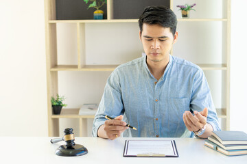 Young Asian lawyer working on financial audit and client support while working hard in the office. Delegate legal concept litigation with hammers and scales placed in front of you.