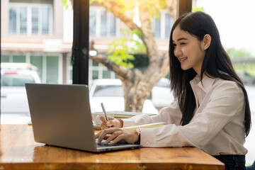 Young Asian students are smiling and looking at the camera in studying the future for themselves or personal learning ideas. Smiling young student studying online at home with books and laptop.