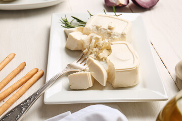 Plate with crushed feta cheese on light wooden background