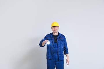 Mature worker in hardhat with flashlight on light background