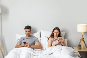 Young couple using mobile phones after quarrel in bedroom