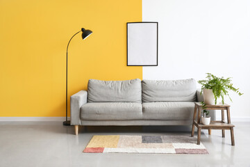 Interior of stylish living room with grey sofa, lamp and blank frame