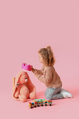 Cute baby girl with toys on color background