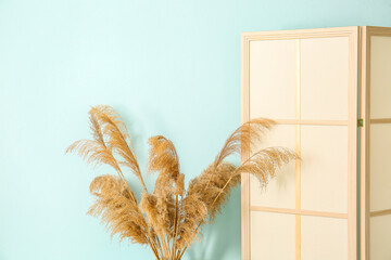 Modern folding screen and pampas grass near blue wall