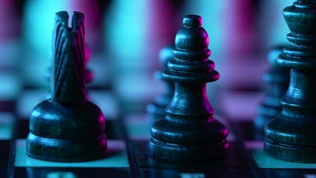Board intelligence game - wooden chess under neon colorful light - pink and blue. Close- up view of pieces on chessboard on dark background. Business solutions, sport, success strategy concept.