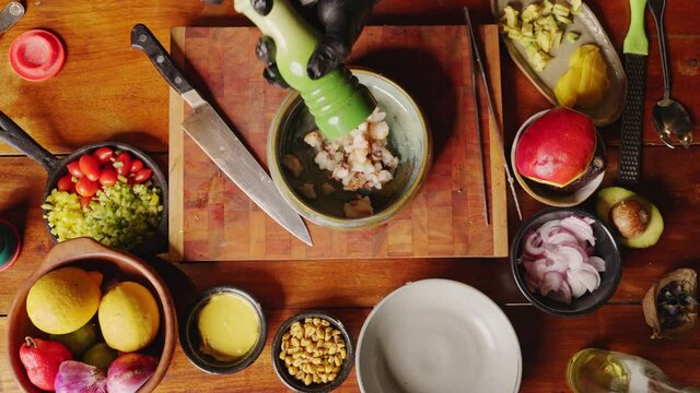 Preparation of Ceviche - straight down view of a professional chef seasoning the dish with salts and peppers, cooking scene concept.