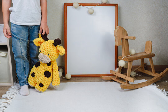 The child is holding a soft toy. Mockup of the picture in the children's room. wooden horse and knitted toys. The boy plays with toys. The interior of the nursery in beige colors.