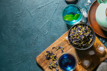 Glass cups of organic blue tea and dried flowers on color background