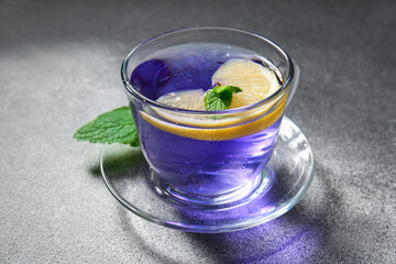 Glass cup of organic butterfly tea and lemon on grey background, closeup