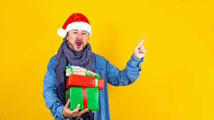 latin senior man holding Christmas presents with santa hat on yellow background in Mexico Latin America	