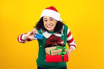Portrait of Latin woman holding Christmas gift box amd credit card for shooping on a yellow background in Mexico latin america	